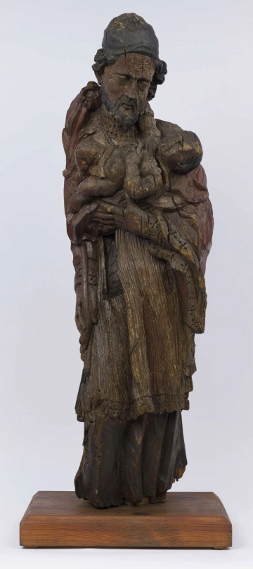 E/17554/ML - Rzeźba drewniana, pełna, z resztkami polichromii, przedstawiająca św. Józefa z Dzieciątkiem. Kompozycja frontalna. Postać stojąca, ubrana w długą szatę wykończoną ozdobną szatę wykończoną ozdobną koronką przy rękawach, drapowane w pionowe fałdy. Na ramionach  płaszcz, również wykończony koronką. Tył postaci modelowany gładko. Prawa ręka, wyciągnięta wzdłuż ciała, trzyma kwiat, który wystaje ponad ramię. Na lewej zgiętej ręce – Dzieciątko, które prawą ręką trzyma się szyi św. Józefa. Dzieciątko nagie, w pieluszkach. 
Twarz świętego skierowana w stronę Dzieciątka, pochylona w prawo. Pociągła. Nos posty. Usta lekko zaznaczone. Oczy lekko przymknięte. Bruzdy na czole i policzkach, misterne pukle brody i włosów. Na głowie rodzaj czapki, ściśle przylegającej. Postać świętego bez stóp. Liczne spękania i ubytki fragmentów.

Konserwacja: 1988 r.