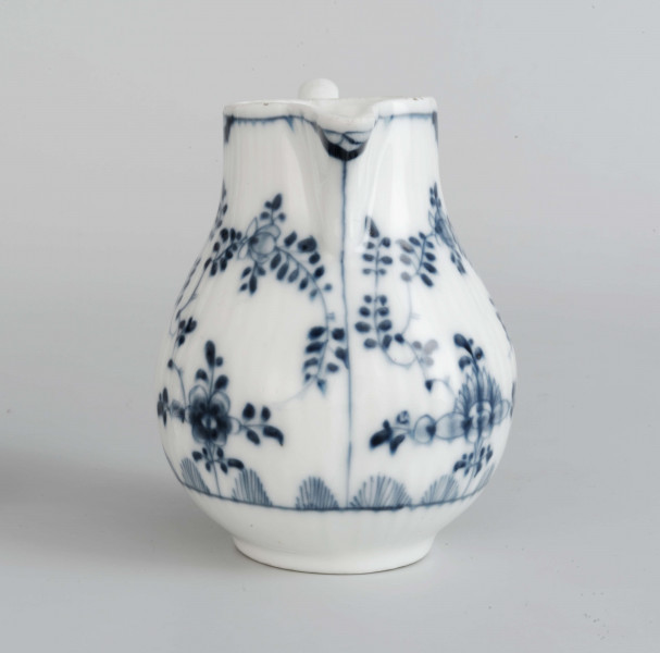 Dzbanek gruszkowaty na niskiej pierścieniowatej podstawie, ucho wolutowe, wylew trókątny, powierzchnia drobno kanelowana. Malowany podszkliwnie błękitem kobaltowym we wzór suchych kwiatów (kocanka), poniżej brzegu górnego na zewnatrz i wewnątrz malowana cienka obwódka, na dnie brzegu uszka gałązka. 
