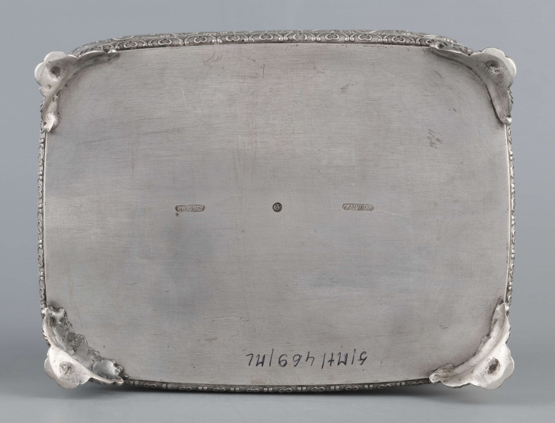 S/Mt/469/ML - Cukiernica prostokątna o zaokrągłonych narożach, profilowana, na czterech akantowych nóżkach. Brzeg dolny i górny obwiedzione półwałkiem zmoletowanej taśmy: u góry z wzorem winorośli, na dole - trójliścia.Brzeg wieczka fasetowany, z przodu lekko wywinięty tworzy uchwyt. Na wieczku nałożona półplastyczna plakieta w postaci  asymetrycznej gałązki kwiatowej. Szyld zamka stanowi sztancowana plakieta z motywem winorośli. Wnętrze złocone.
Na dnie sygnatura wypukła we wklęsłych ramkach:
- J.Suchocki
- w Lublinie
i punca z oznaczeniem próby 