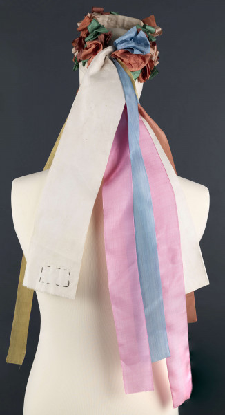 E/5038/ML - Strój głowy panny młodej wykonany jako rekonstrukcja. Wianek z papieru obszytego białym płótnem fabrycznym.  Z  wierzchu naszyte kolorowe wstążki poskładane i pozszywane na krzyż. W tyłu doszyte długie kolorowe wstążki, koloru: czerwonego, różowego, zielonego i niebieskiego.  