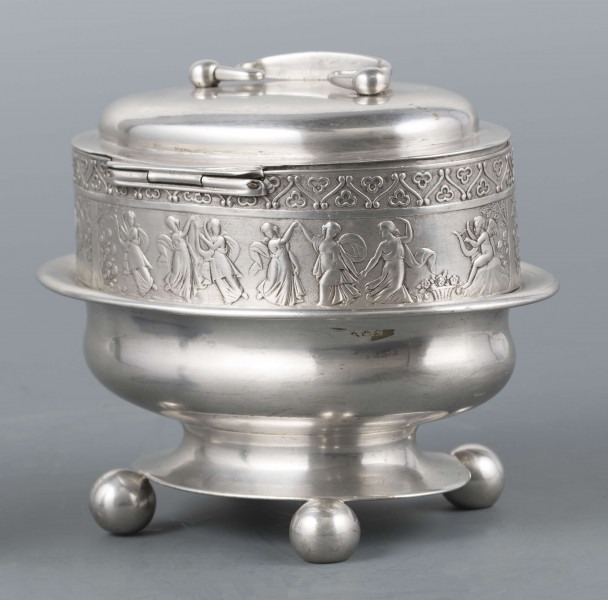 S/Mt/363/ML - Cukiernica owalnana niskiej stopie z czterema kulistymi nóżkami, z pokrywką w formie wieczka.
Podzielona na dwie części : 
- część dolna lekko wybrzuszona, o gładkiej powierzchni, kończy się w połowie wysokości wywiniętym kołnierzem; - część górna prosta uformowana jest z moletowanej taśmy, na której powtarza się trzykrotnie scenka antyczna: po rawej siedzący pod drzewem amorek gra na lirze, po lewej stoi grająca na lirze kobieta, pomiędzy nimi tańczą trzy inne.Górną krzwędź obiega pas stylizowanych neogotyckich trójliści.