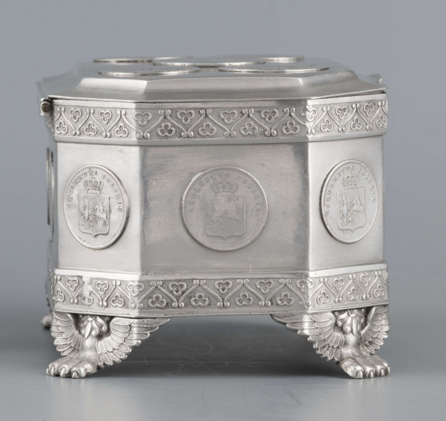 S/Mt/364/ML - Cukiernica skrzynkowa prostokątna ze ściętymi narożami, na czterech nóżkach w formie uskrzydlonych lwich łap, z wieczkiem o wklęsło profilowanym brzegu. Górny i dolny brzeg obiega  moletowana taśma z motywem neogotyckich trójliści, szyld zamka ma formę różanego wieńca pod skrzydatą główką..W ścianki i wieczko wmontowanych jest 15 monet srebrnych:
1 ort Zygmunta III
1 talar pruski, 1818 r.
1 pięciofrankówka, 1811 r.
1 moneta austriacka, 1797 r.
1 moneta saska, 
2 monety polskie St.Augusta Poniatowskiego
1 dwózłotówka Królestwa Polskiego, 1825 r.
1 pięciozłotówka, 1831 r.
6 złotówek, 1831 r.
Na dnie sygnatura wklęsła kursywą:
- K. Rotkiel w Lublinie
i punca z oznaczeniem próby 