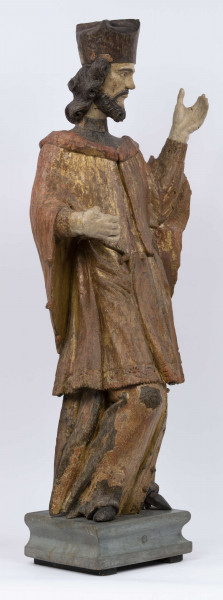 E/16816/ML - Rzeźba drewniana, pełna, polichromowana, przedstawiająca św. Jana Nepomucena. Kompozycja frontalna. Postać stojąca w kontrapoście – prawa noga zgięta i wysunięta do przodu. Sylwetka przechylona na prawo. Lewa ręka zgięta w łokciu i wysunięta do przodu. Prawa zgięta, uniesiona do góry. Brak atrybutów (krzyża i palmy) w dłoniach.
Postać ubrana w sutannę, komżę drapowaną w fałdy i zakończoną koronką, płaszcz z kapturem. Ślady złoceń na partii ubrania. Głowa skierowana na prawo. Twarz podłużna (kolor kremowy), usta proste, oczy z zaznaczonymi na ciemno tęczówkami, nos prosty, lekko zaznaczone kości policzkowe. Wolutowe pukle brody i włosów, symetryczne. Na głowie ciemnobrązowy biret. Stopy wystające spod sutanny.

Konserwacja: 2001 r.