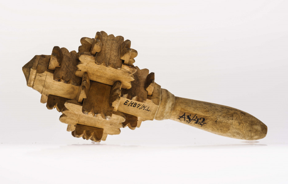 Grzechotka ta składa się z kawałeczków deseczki, rzeźbionych z brzegu i wycinanych w środku z jednej strony. Zrobiona jest bez kleju i gwożdzi. Deseczki te mają wymiary: dł. 4,5 cm szer. 2,2 cm grub. 0,5 cm. Jest ich 26. Tworzą one 6 