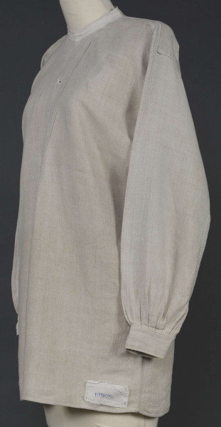 E/7980/ML - Koszula męska z lnianego, szarego płótna. Szyta ręcznie. Kołnierzyk to wąska oszewka z bawełnianego płótna. Z przodu rozcięcie zapinane na 3 guziczki wzmocnione plisą z podwójnego kawałka płótna. Rękawy długie, ujęte w mankiet, zapinany na guziczek. Pod pachami wszyte prostokątne kawałki tkaniny, zw. tokami.