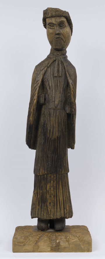 E/8386/ML - Rzeźba drewniana, pełna, niepolichromowana, przedstawiająca świętego. Twarz owalna o pucułowatych policzkach. Oczy owalne, brwi łukowate zbiegające się i nasady nosa. Nos krótki, prosty. Mała broda i sumiaste wąsy, otulają usta. Broda i wąsy podkreślone pionowymi żłobieniami. Włosy z grzywką na czole, z tyłu sięgają do karku. Fryzura podkreślona  żłobieniami, dość sztywna. Święty w długiej sukni, komży i pelerynie. Szaty podkreślone pionowymi żłobieniami. Na szyi  przewieszona stuła. Peleryna z odwiniętymi połami, pod brodą zawiązana tasiemką. Brak rąk. Czubek głowy uszkodzony. 

Konserwacja: 1990 r.