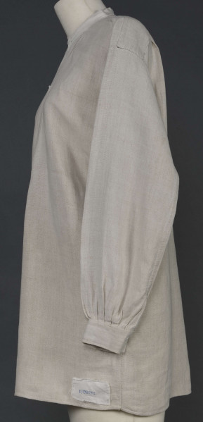 E/7980/ML - Koszula męska z lnianego, szarego płótna. Szyta ręcznie. Kołnierzyk to wąska oszewka z bawełnianego płótna. Z przodu rozcięcie zapinane na 3 guziczki wzmocnione plisą z podwójnego kawałka płótna. Rękawy długie, ujęte w mankiet, zapinany na guziczek. Pod pachami wszyte prostokątne kawałki tkaniny, zw. tokami.