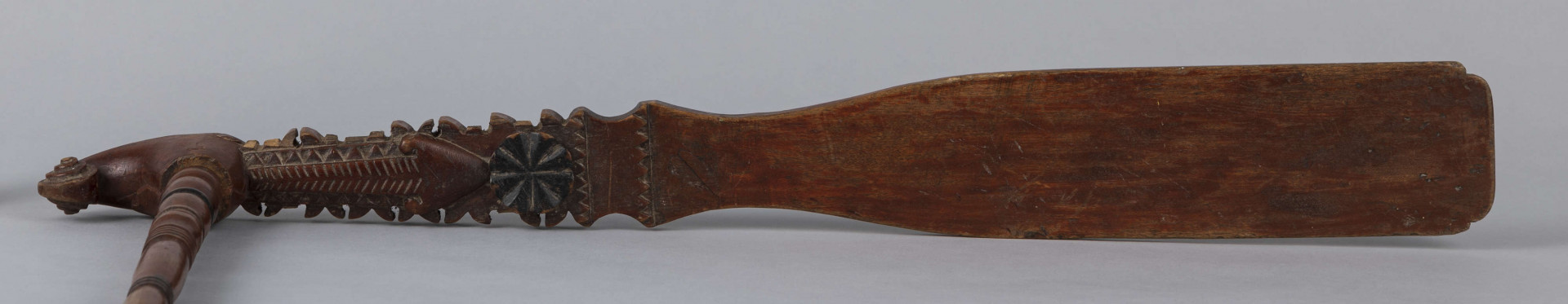 E/9283/ML - Przęślica drewniana wykonana z 3 części. Przysiadka w formie płaskiej deszczułki zwężająca się w jednym końcu i zdobiona snycerką: rozeta, motyw sercowaty, ząbki. Jej ostre zakończenie ma formę woluty/ślimaka. Przy węższym końcu osadzone pionowo ramię, toczone w pierścieniowate ozdoby. Na niego nakładany ruchomy krężel, również w toczony w pierścieniowate ozdoby. Przęślica powleczona brązowo-wiśniową farbą. Pierścieniowate elementy malowane na czarno, a na krężlu dodatkowo na srebrno.