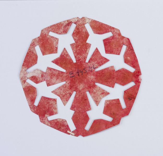 Wycinanka czerwona w formie ośmioboku, w centrum kwiat o trapezowatych płatkach, przedłużenie, których stanowią romby, otok z rombów i ściętych stożków.