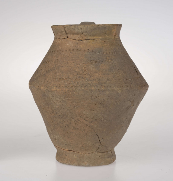 Dzban ostro profilowany, z prostym, odgiętym na zewnatrz brzegiem podkreślonym rowkiem, ostro zaznaczonym załomem brzuśca i wyodrębioną stopką. Ucho dzbana jest taśmowate, kolankowato zgięte, z przewierconym kanalikiem. Ponad załomem brzuśca naczynie zdobione jest ornamentem blankowym, który tworzy para równolegle rytych linii wypełnionych dołkami. Całość ujęta górą i dołem w wątek linii rytej i rzędu dołków. 
