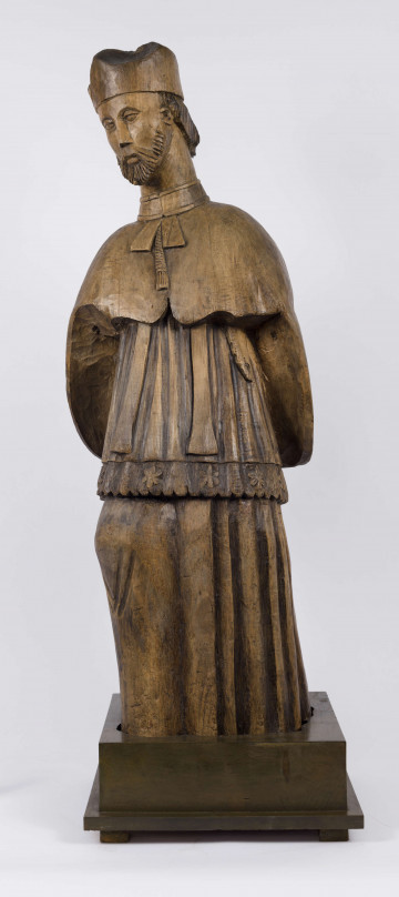 E/1957/ML - Rzeźba drewniana, niepolichromowana, zakomponowana frontalnie. Przedstawia postać Świętego. Głowa lekko pochylona w prawo. Twarz owalna, brwi wąskie łukowate. Oczy lekko opuszczone w dół. Nos wąski, prosty. Krótka broda okala twarz. Widoczne spod biretu włosy sięgają do karku i podkreślone są pionowymi żłobieniami. Postać w sutannie, komży i pelerynie. Spod sutanny widoczne lekko zgięte i wysunięte prawe kolano. Komża ułożona w fałdy, u dołu wycięta „w ząbki”. Wzdłuż krawędzi komży zdobiony pas kwiatowy. Spod peleryny widoczna stuła.

Konserwacja: 2004-2005