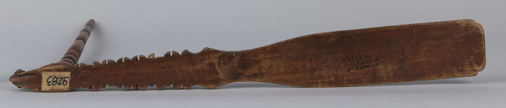 E/9283/ML - Przęślica drewniana wykonana z 3 części. Przysiadka w formie płaskiej deszczułki zwężająca się w jednym końcu i zdobiona snycerką: rozeta, motyw sercowaty, ząbki. Jej ostre zakończenie ma formę woluty/ślimaka. Przy węższym końcu osadzone pionowo ramię, toczone w pierścieniowate ozdoby. Na niego nakładany ruchomy krężel, również w toczony w pierścieniowate ozdoby. Przęślica powleczona brązowo-wiśniową farbą. Pierścieniowate elementy malowane na czarno, a na krężlu dodatkowo na srebrno.