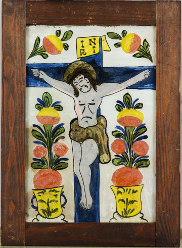 Obraz na szkle. Oprawiony w ramki. Tematem jest Chrystus na krzyżu. Tło jasne, krzyż koloru ciemnoniebieskiego. Z obu stron krzyża umieszczone są w żółtych wazonikach (jeden ma ucha) stylizowane motywy roślinne (kwiaty lub owoce) koloru różowego, żółtego, zielonego i niebieskiego. Podobne motywy  roślinne znajdują się także na obu ramionach krzyża. Postać Chrystusa traktowana bardzo schematycznie. Zarówno kształt, jak i twarz, zaznaczone są kilkoma kreskami. Ciało modelowane farbą. Artysta użył tu prymitywnego światłocienia. Ciało ma kolor szary, miejscami różowy, włosy brązowe, nimb i krótkie perizonium złote. Światłocień występuje także na krzyżu, na którym artysta chciał oddać cień padający od postaci Chrystusa; cień kolor granatowego. Tablica nad głową żółkła. Linie rysunku dość grube.