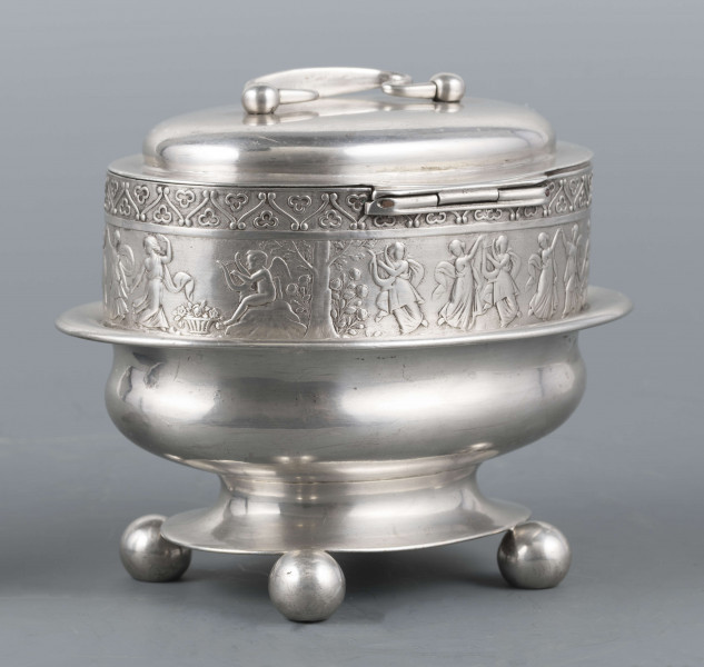 S/Mt/363/ML - Cukiernica owalnana niskiej stopie z czterema kulistymi nóżkami, z pokrywką w formie wieczka.
Podzielona na dwie części : 
- część dolna lekko wybrzuszona, o gładkiej powierzchni, kończy się w połowie wysokości wywiniętym kołnierzem; - część górna prosta uformowana jest z moletowanej taśmy, na której powtarza się trzykrotnie scenka antyczna: po rawej siedzący pod drzewem amorek gra na lirze, po lewej stoi grająca na lirze kobieta, pomiędzy nimi tańczą trzy inne.Górną krzwędź obiega pas stylizowanych neogotyckich trójliści.