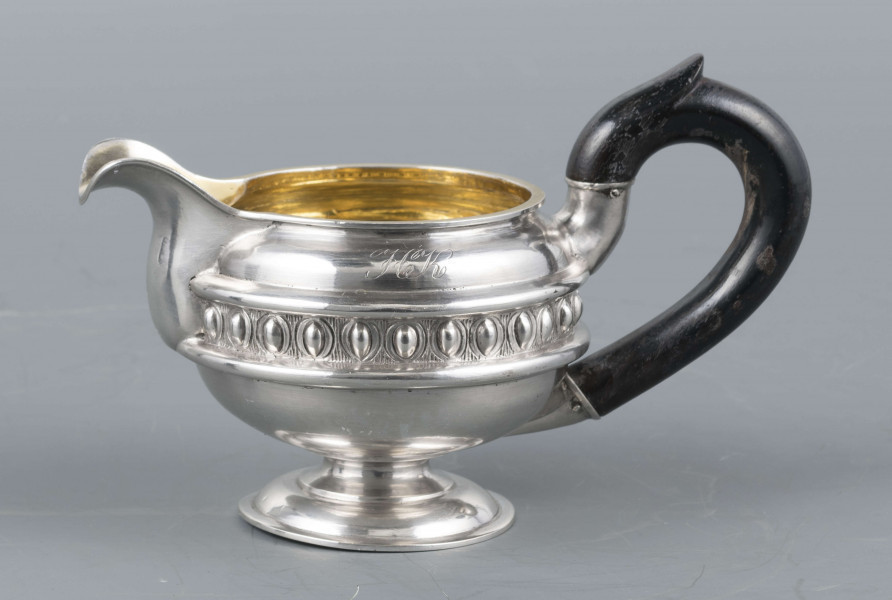 S/Mt/545/ML - Brzusiec w formie spłaszczonej kuli, pośrodku zdobiony repusowanym pasem kimationu obwiedzionego dwoma półwałkami, brzeg górny z okrągłym rantem, wylew wywinięty, zaokrąglony. Wnętrze złocone. Stopa okrągła profilowana, ucho drewniane malowane na czarno, osadzone w dwóch tulejkach . Na brzuscu pod górną krawędzią grawerowany ozdobny monogram 