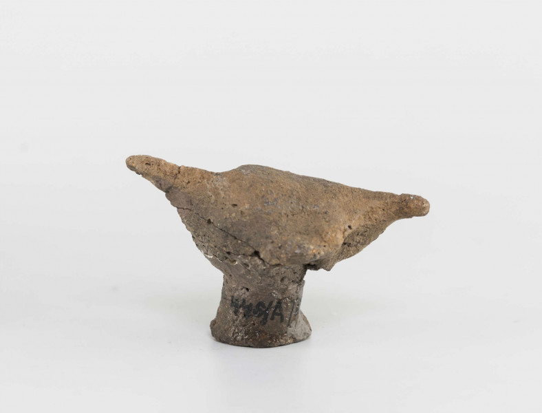 Figurka zoomorficzna w kształcie ptaszka, wykonana schematycznie. Nóżka walcowata. Główka, ogon oraz skrzydełka ledwie zaznaczone. Powierzchnia gładzona niestarannie. Sklejone, uzupełnione gipsem. Surowiec - glina z domieszką drobnoziarnistą. Barwa Szarobrunatna. Wypał dobry.
Wymiary dodatkowe: 1,3 cm (śr. stopki), 2,4 cm (rozstaw skrzydełek)