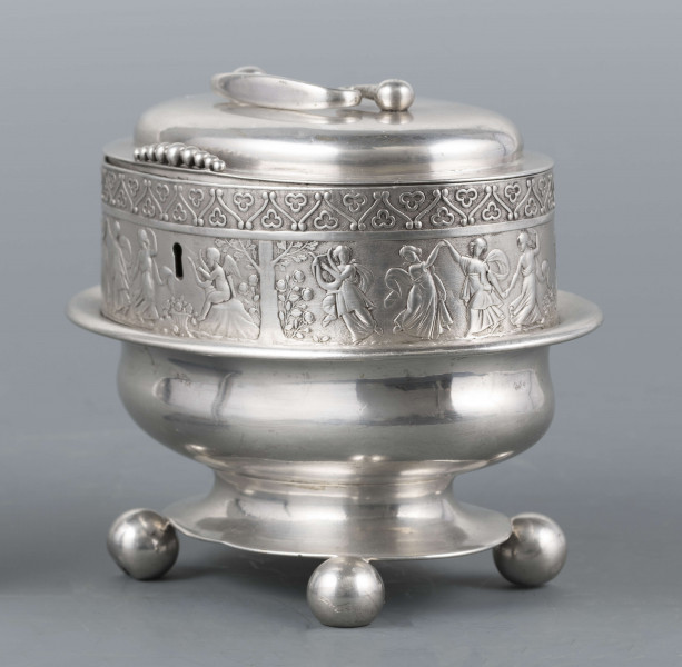 S/Mt/363/ML - Cukiernica owalnana niskiej stopie z czterema kulistymi nóżkami, z pokrywką w formie wieczka.
Podzielona na dwie części : 
- część dolna lekko wybrzuszona, o gładkiej powierzchni, kończy się w połowie wysokości wywiniętym kołnierzem; - część górna prosta uformowana jest z moletowanej taśmy, na której powtarza się trzykrotnie scenka antyczna: po rawej siedzący pod drzewem amorek gra na lirze, po lewej stoi grająca na lirze kobieta, pomiędzy nimi tańczą trzy inne.Górną krzwędź obiega pas stylizowanych neogotyckich trójliści.