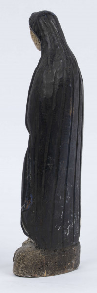 E/6363/ML - Rzeźba z drewna lipowego, polichromowana farbą olejną. Zakomponowana w jednym kawałku drewna na postumencie o formie owalnej z płaskorzeźbionym motywem dwóch skrzyżowanych gałęzi. Postać stojąca przedstawia Matkę Boską Różańcową. Twarz owalna, głęboko osadzone oczy, prosty i szeroki nos, małe pełne usta. Ręce zgięte w łokciach: duże dłonie złożone do modlitwy. Na przedramieniu prawej ręki brązowy różaniec o płaskich paciorkach, zakończony dużym krzyżem. Postać odziana w białą prostą suknię, gładko wykończoną pod szyją i przewiązaną granatową szarfą. Na głowie granatowa szata spełniająca jednocześnie rolę peleryny spływającej z ramion ku dołowi i spowijającej całą postać.