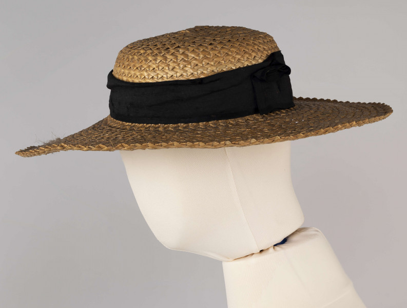 E/586/ML - Kapelusz ze słomy żytniej, o owalnym denku i płaskim rondzie. Upleciony techniką warkoczową - warkocze wąskie, ząbkowane, zszyte szarymi nićmi. Denko otoczone czarną, jedwabną wstążką o szerokości 5 cm.
