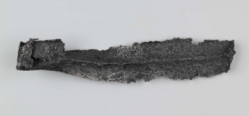 Żelazny grot oszczepu z ostrym żeberkiem środkowym, zgięty rytualnie. Grot stanowi element wyposażenia ciałopalnego pochówku złożonego prawdopodobnie w popielnicy. Odkrycia dokonano w 1959 roku przypadkowo w czasie prac rolnych. Oprócz trzech grotów, pochówkowi wojownika towarzyszyły: żelazne umbo, dwie ostrogi, tok brązowy (prawdopodobnie okucie drzewca oszczepu) a także żelazny miecz z miedziana inkrustacją wyobrażającą rzymskich bogów. Pochowany na terenie obecnej wsi Podlodów wojownik należał do elity wojskowej przedstawicieli kultury przeworskiej.