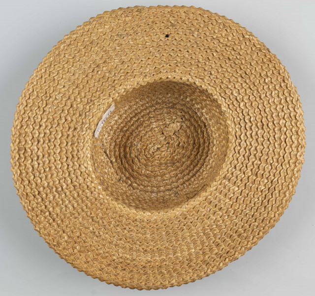 E/586/ML - Kapelusz ze słomy żytniej, o owalnym denku i płaskim rondzie. Upleciony techniką warkoczową - warkocze wąskie, ząbkowane, zszyte szarymi nićmi. Denko otoczone czarną, jedwabną wstążką o szerokości 5 cm.
