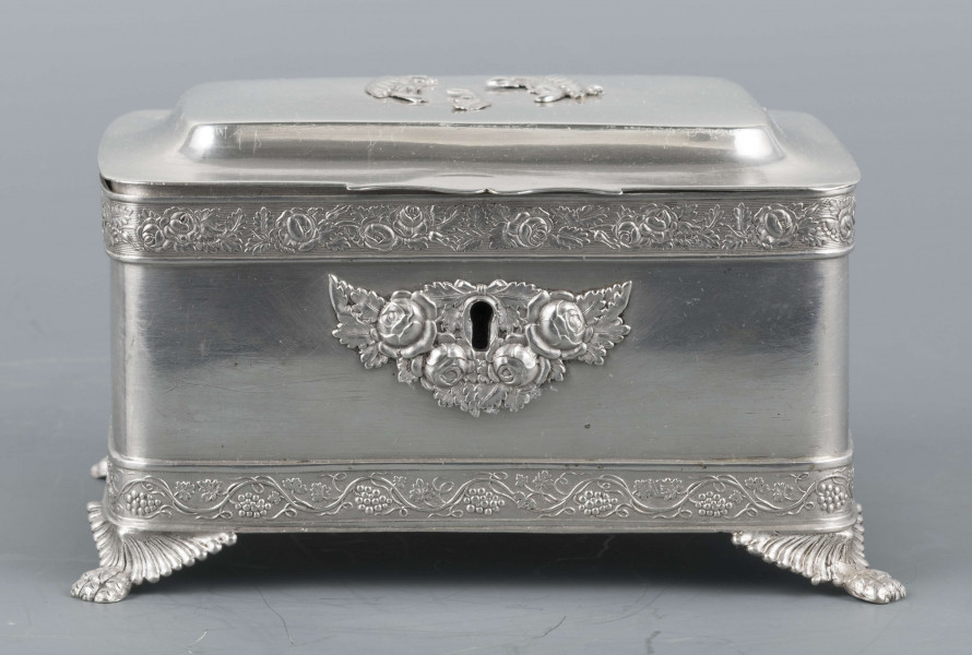 S/Mt/354/ML - Cukiernica prostokątna o lekko zaokrąglonych narożach, na czterech nóżkach w formie uskrzydlonych lwich łap, z profilowanym wieczkiem. Brzegi obwiedzione moletowaną taśmą: u dołu z motywem winnej łozy, u góry - wici różanej.Szyld zamka zdobi plakieta z girandą róż, druga - na wieczku - jest uszkodzona a przez to nieczytelna.
Na dnie sygnatury kursywa we wklesłych owalnych ramkach:
- K.Rotkiel
- w lublinie
Przedzielone okrągłą puncą z próbą 