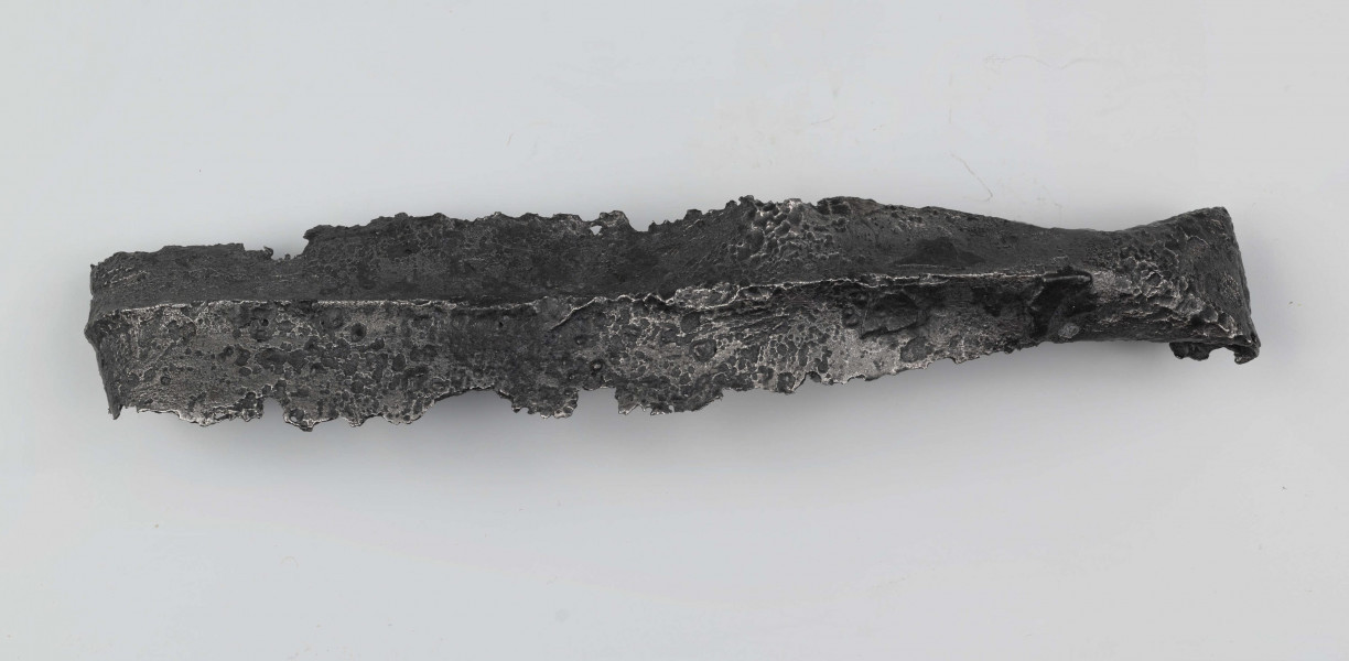 Żelazny grot oszczepu z ostrym żeberkiem środkowym, zgięty rytualnie. Grot stanowi element wyposażenia ciałopalnego pochówku złożonego prawdopodobnie w popielnicy. Odkrycia dokonano w 1959 roku przypadkowo w czasie prac rolnych. Oprócz trzech grotów, pochówkowi wojownika towarzyszyły: żelazne umbo, dwie ostrogi, tok brązowy (prawdopodobnie okucie drzewca oszczepu) a także żelazny miecz z miedziana inkrustacją wyobrażającą rzymskich bogów. Pochowany na terenie obecnej wsi Podlodów wojownik należał do elity wojskowej przedstawicieli kultury przeworskiej.