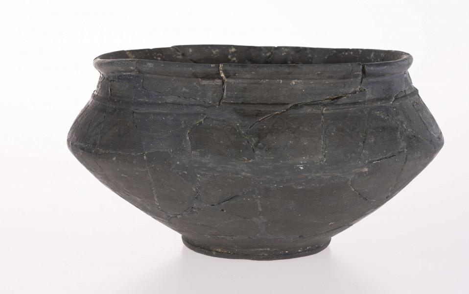 Naczynie wazowate - dwustożkowate; dno lekko wklęsłe z dołeczkiem w środku, wyraźnie wyodrębnione niewielką stopką; brzusiec dwustożkowaty, ostro profilowany; miejsce przejścia brzuśca w szyję zaznaczone wypukłą dookolna listwą; szyja niska, cylindryczna; wylew zaokrąglony, wywiniety na zewnatrz; górna część brzuśca zdobiona dookolnym rzędem narysowanych 