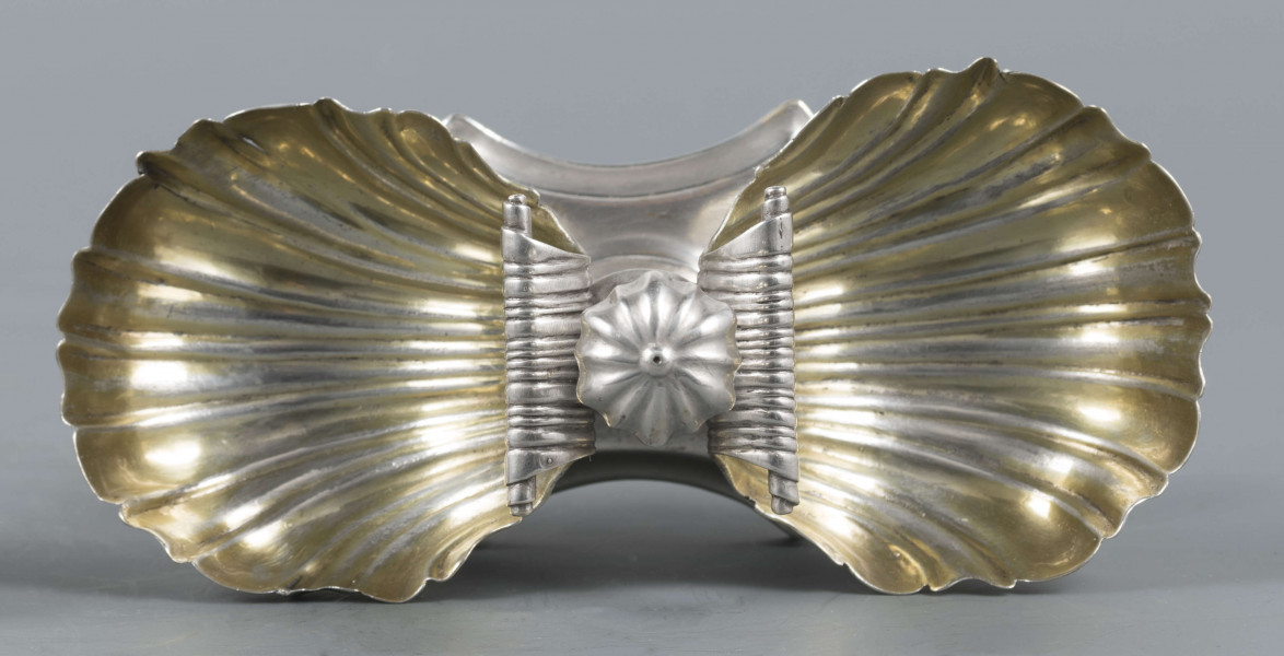 S/Mt/494/ML - Solniczka składa się z dwóch czarek w formie muszli połączonych z pionowym, profilowanym uchwytem o zwieńczniu w formie makówki ustawionym na wydłużonej ośmiobocznej podstawie o wklęsłych bokach. Krawędź podstawy fasetowana, boki karbowane, cztery nóżki w kształcie spłaszczonych kulek. Wnetrze muszli złocone.
Na dnie podstawy sygnatura kursywą w owalnych ramkach:
- J.Gałecki
- w Lublinie
- punca owalna z przedstawieniem dłoni (sygnatura pomocnicza)
- wężyk probierczy
- znak probierni warszawskiej z próbą 