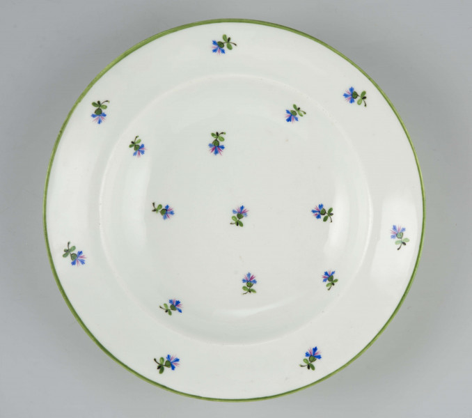 Talerz głęboki, okrągły, gładki, zdobiony malowanym rzutem drobnych chaberków z błękitnymi kwiatkami i zielonymi listkami, krawędź obwiedziona zielonym konturem.
Na spodzie malowane znaki:
 