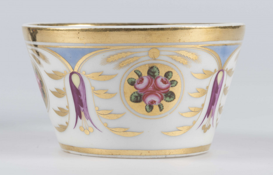 S/CS/1388/3/ML - Filiżanka koniczna, ucho łamane, profilowane, z przewiązkami w osadzeniach.  Dekoracja malowana wielobarwnie i złocona: brzusiec obiega szeroki fryz złożony ze stylizowanych ornamentów roślinnych (gałązek, kłosów zbóż i liści akantu)  połączonych z owalnymi medalionami, w których są trzy różowe różyczki z zielonymi listkami na złotym tle. Wylew złocony, złotym konturem obwiedzione ucho.
 