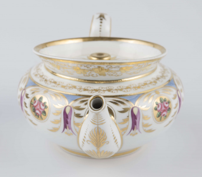 S/CS/1388/1/ML - Brzusiec w formie spłaszczonej kuli, ucho zaokrąglone wyciągnięte ponad górną  krawędź, dziobek lekko wygięty osadzony w dolnej połowie korpusu i uniesiony ku górze. Wokół wylewu wysoki kołnierz ze skośnym ścięciem wyżej uniesionym od strony dziobka, z odchylonymi na zewnątrz ściankami. Pokrywka płaska z uchwytem w postaci płaskiego guzika. Dekoracja malowana wielobarwnie i złocona: brzusiec obiega szeroki fryz złożony ze stylizowanych ornamentów roślinnych (gałązek, kłosów zbóż i liści akantu)  połączonych z owalnymi medalionami, w których są trzy różowe różyczki z zielonymi listkami na złotym tle. Krawędź górną i boki kołnierza obiega ornamentalna złota bordiura, na pokrywce stylizowana złota rozeta, złotym konturem obwiedzione wszystkie krawędzie.
 