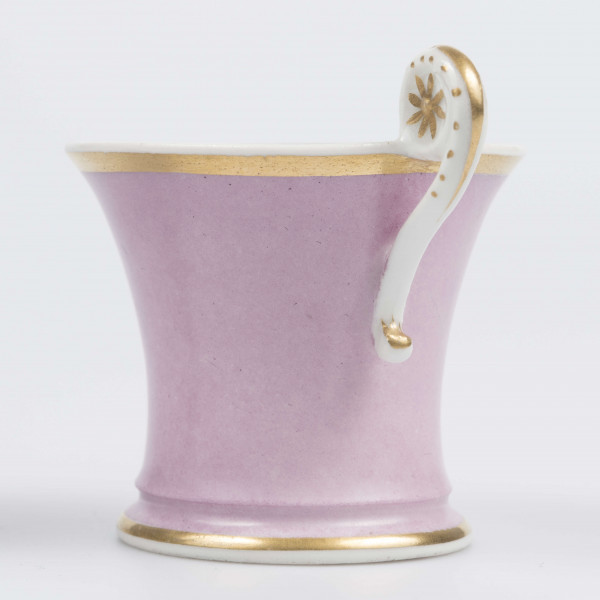 S/CS/133/1/ML - Filiżanka koniczna z rozchylonym wylewem, na niskiej stopie, ucho w formie pastorału z wolutą wyciągnietą ponad krawędź wylewu, zdobioną reliefową rozetką. Powierzchnia matowa malowana w całości na liliowy kolor, wylew obustronnie obwiedziony złotym paskiem, złotym konturem podkreślony brzeg stopy i profile ucha.
