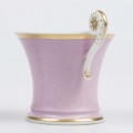 S/CS/133/1/ML - Filiżanka koniczna z rozchylonym wylewem, na niskiej stopie, ucho w formie pastorału z wolutą wyciągnietą ponad krawędź wylewu, zdobioną reliefową rozetką. Powierzchnia matowa malowana w całości na liliowy kolor, wylew obustronnie obwiedziony złotym paskiem, złotym konturem podkreślony brzeg stopy i profile ucha.
