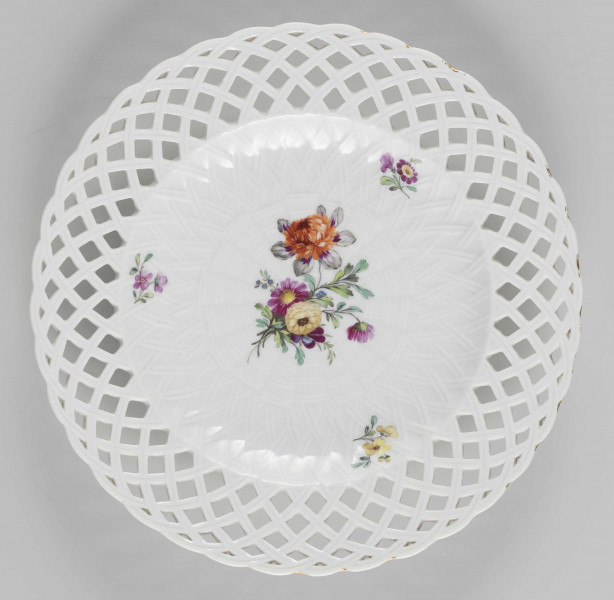 S/CS/1488/ML - Talerz płytki pokryty reliefową plecionką koszykową, w partii kołnierza ażurowo wyciętą. Układ  plecionki  tworzy falistą  linię brzegu. Na dnie malowany wielobarwnie pęk fantazyjnych  kwiatów  i trzy małe kwiatowe gałązki, na spodzie kołnierza zielona gałązka z listkami. 
 