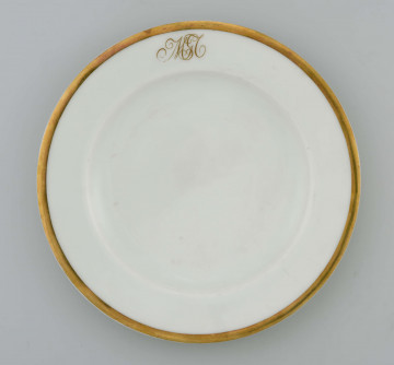 Talerz płytki, okrągły, gładki, brzeg obwiedziony szerokim złotym paskiem, na kołnierzu złoty monogram wiązany 