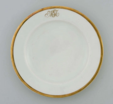 Talerz płytki, okrągły, gładki, brzeg obwiedziony szerokim złotym paskiem, na kołnierzu złoty monogram wiązany 