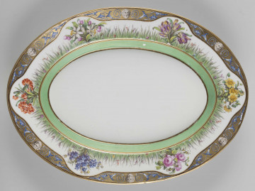 S/CS/1545/ML - Półmisek owalny, wgłębiony, dekoracja malowana wielobarwnie. Faseta w kolorze jasnej zieleni ujęta w złote kontury. Na kołnierzu wzór traw z drobnymi kwiatkami, pośród nich 6 większych bukietów kwiatowych (róże, tulipany, goździki i in.), wokół brzegu złoty fryz z antykizującymi ornamentami złożonymi z brodatych maszkaronów 