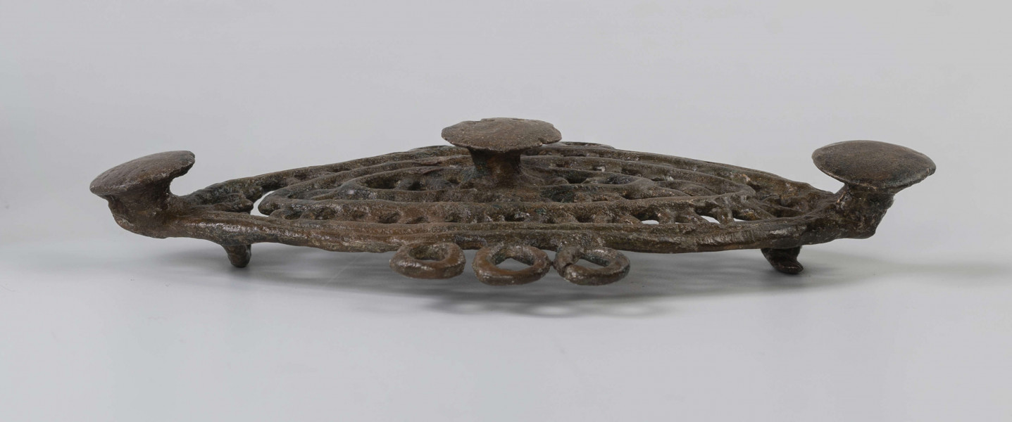 1396/A/ML/2 - Ażurowa fibula z brązu będąca elementem dwuczęściowej ozdoby. Na ornament składają się trzy koncentryczne listwy soczewkowate połączone ze sobą naprzemianlegle skośnymi, krótkimi poprzeczkami, tworzącymi trójkąty. Na dłuższej osi tarczki umieszczone są trzy symetrycznie guzki. Po środku dłuższych boków tarczki, naprzeciw siebie znajdują się potrójne uszka. 