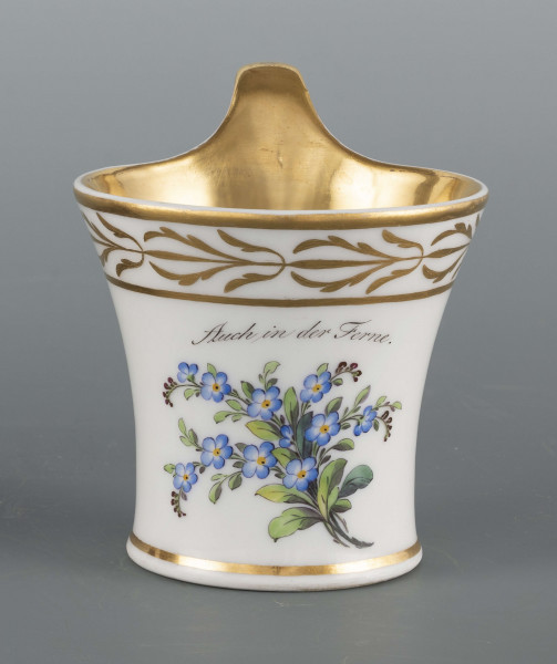 S/CS/145/ML - Filiżanka koniczna, ucho pętelkowe. Dekoracja malowana wielobarwnie i złocona. Frontalnie na białym tle malowany bukiet niezapominajek a nad nim napis złotem 