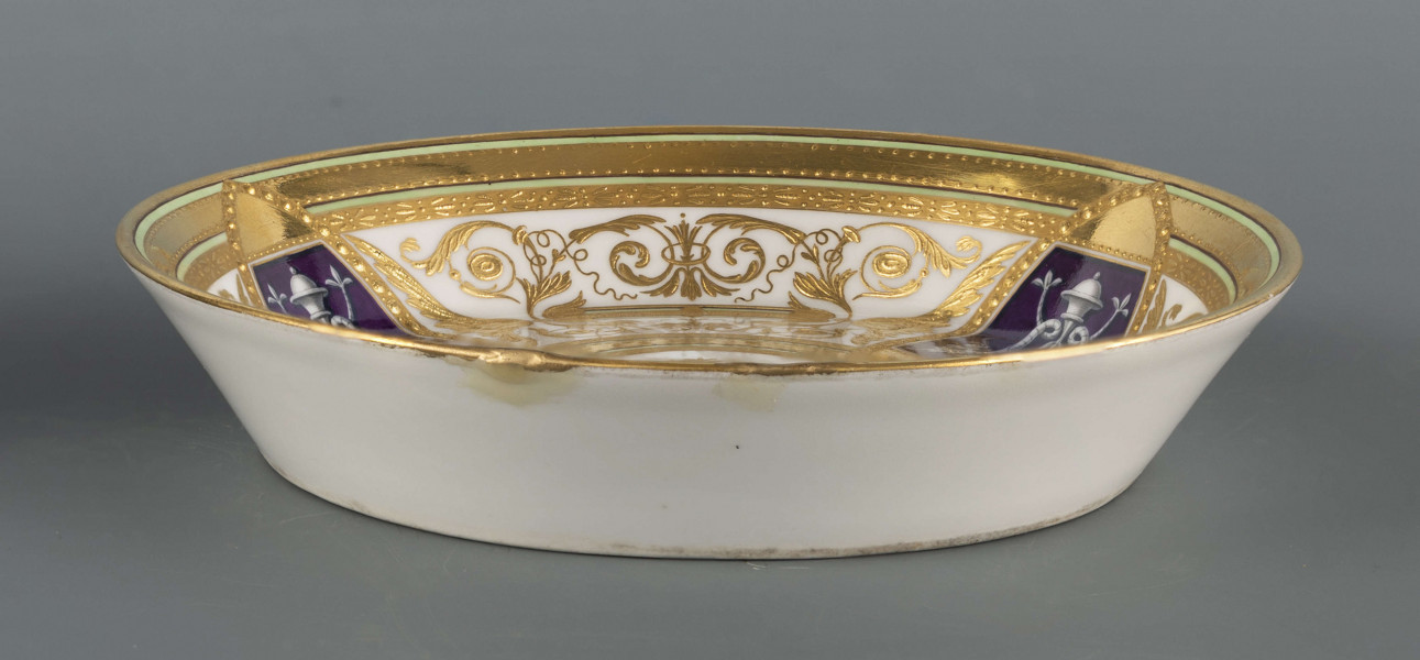 S/CS/1160/ML - Spodek okrągły, konicznie wgłębiony,  na nim bogata dekoracja w wypukłym złocie z ornamentów groteskowych, perełek i wzorów geometrycnych, ułożona w koncentryczne kręgi przedzielone wąskimi paskami jasnej zieleni, z rozetą pośrodku. Na kołnierzu wydzielone 3 migdałowate medaliony, wewnątrz nich mianiatury en grisaille na liliowym tle przedstawiające dwa połączone maszkarony 
  