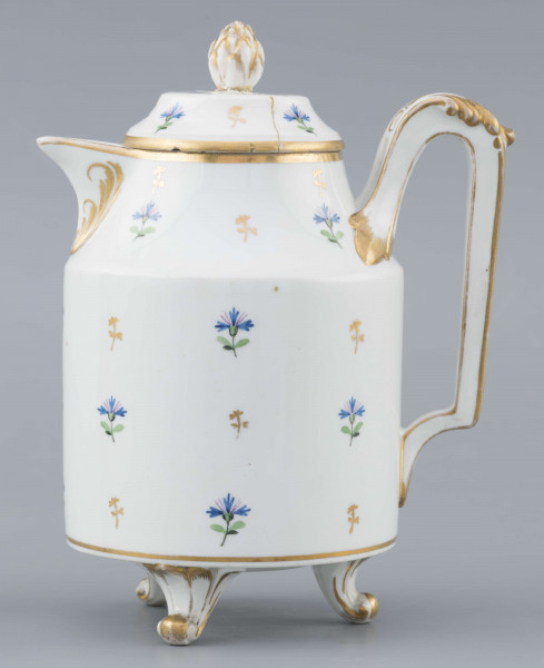 S/CS/1511/ML - Dzbanek cylindryczny, na trzech nóżkach w kształcie lwich łap, szyja w formie zwężonego pierścienia, wylew z dziobkiem, ucho dołem prostokątnie załamane, górą wygięte, rozdwojone, z reliefowymi liśćmi w osadzeniach. Przykrywa w formie wąskiego, konicznego pierścienia, z uchwytem w kształcie szyszki. Dekoracja malowana: regularny rzut drownych chabrów w kolorach błękitu i zieleni. Krawędzie,  ucho, dziobek, nóżki i uchwyt pokrywki konturowane złotem.
