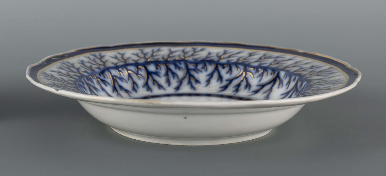 S/CS/1401/ML - Talerz głęboki, okrągły, z wodrębnioną fasetą, brzeg kołnierza falisty. Zdobiony malowanym wzorem kobaltowym i złoceniem: na kołnierzu i fasecie nieulistnione gałązki stylizowanej tarniny konturowane złotem, w tle złota siateczka, ujęte w szerokie kobaltowe obwódki. 
 
