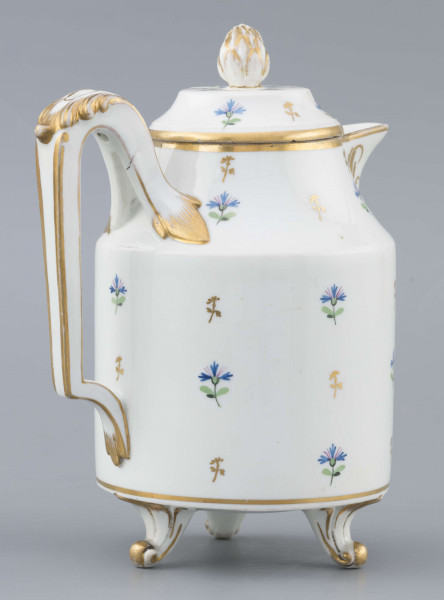 S/CS/1511/ML - Dzbanek cylindryczny, na trzech nóżkach w kształcie lwich łap, szyja w formie zwężonego pierścienia, wylew z dziobkiem, ucho dołem prostokątnie załamane, górą wygięte, rozdwojone, z reliefowymi liśćmi w osadzeniach. Przykrywa w formie wąskiego, konicznego pierścienia, z uchwytem w kształcie szyszki. Dekoracja malowana: regularny rzut drownych chabrów w kolorach błękitu i zieleni. Krawędzie,  ucho, dziobek, nóżki i uchwyt pokrywki konturowane złotem.
