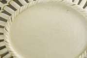Dno płaskie, owalne, w lustrze reliefowy wzór plecionki koszykowej. Kołnierz ażurowy z pionowych spłaszczonych prętów zawiniętych wokół profilowanej obręczy tworzącej krawędź i przeplecionych przez środek podwójnym wałkiem. Pokryty szkliwem w kolorze kości słoniowej.
 