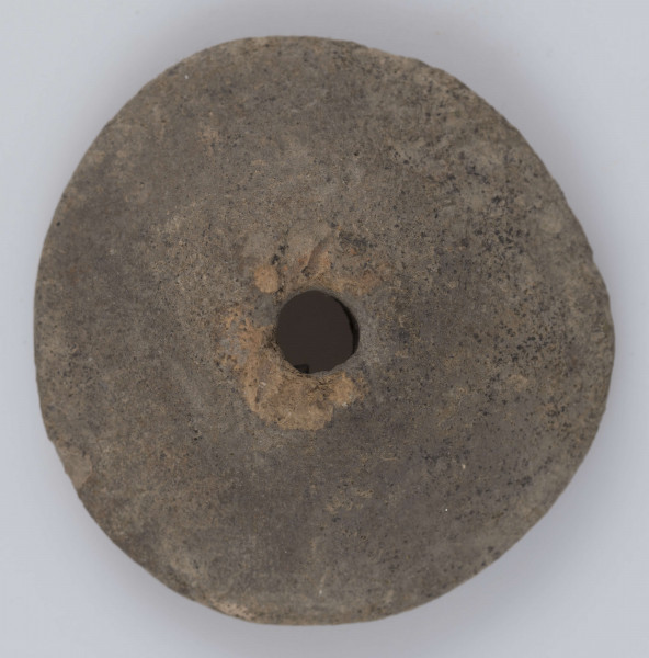 1811/A/ML/3 - Przęślik wklesło wypukły o łukowatej krawędzi; otwór stożkowaty (szerszy po stronie wklęsłej). Barwa powierzchni wypukłej - szara; powierzchni wklęsłej - jasno brunatna. Przełom niewidoczny. Surowiec - glina z drobnym piaskiem. Wypał dobry. 