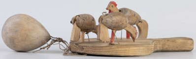 E/17030/ML - Zabawka drewniana przedstawiająca trzy kurki przymocowane do owalnej deseczki z uchwytem. Kurki mają ruchome głowy i ogony, które poruszają się za pomocą sznurków przeciągniętych przez deseczkę i przywiązanych do drewnianej kuli. Deseczka wykonana z drewna sosnowego, kurki z drewna lipowego. Głowy i nogi kurek pomalowane są czerwoną farbą, tułowia zdobi ornament geometryczny w postaci zygzakowatych linii wykonanych brązową farbą.