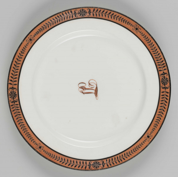 S/CS/1224/ML - Talerz płytki, okgły, gładki, przy krawędzi malowana bordiura ze stylizowanych czarnych gałązekprzedzielonych rozetkami,  na ceglastoczerwonym tle. W lustrze wiązany monogram 