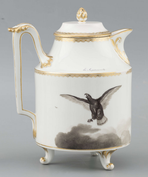 S/CS/1480/ML - Dzbanek cylindryczny, na trzech nóżkach w kształcie lwich łap, szyja w formie zwężonego pierścienia, wylew z dziobkiem, ucho dołem prostokątnie załamane, górą wygięte, rozdwojone, z reliefowymi liśćmi w osadzeniach. Przykrywa w formie wąskiego, konicznego pierścienia, z uchwytem w kształcie szyszki. Dekoracja drukowana en grisaille w kolorze czarnym. Po obu stronach brzuśca sceny alegoryczne: lew prowadzony na pasku przez amorka, powyżej napis 