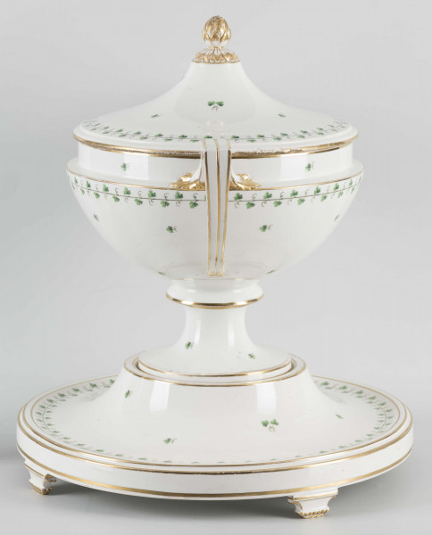 S/CS/1231/ML - Waza półkulista z przewężeniem poniżej wylewu, ucha łamane, stopa o okrągłej podstawie i wąskim trzonie wywiniętym u góry, pokrywa w formie wyniesionego stożka z plastycznym zwieńczeniem i uchwytem w kształcie szyszki. Dekoracja barwnie malowana i złocona: brzusiec, pokrywa i podstawa obwiedzione fryzem winorośli, na powierzchni rytmicznie rozrzucone pojedyncze liski, krawędzie, ucha i uchwyt pokrywy konturowane złotem, 
Podstawa w formie wyniesionego ściętego stożka z okrągłym wgłębieniem u góry, na trzech kostkowych nóżkach. 
 
